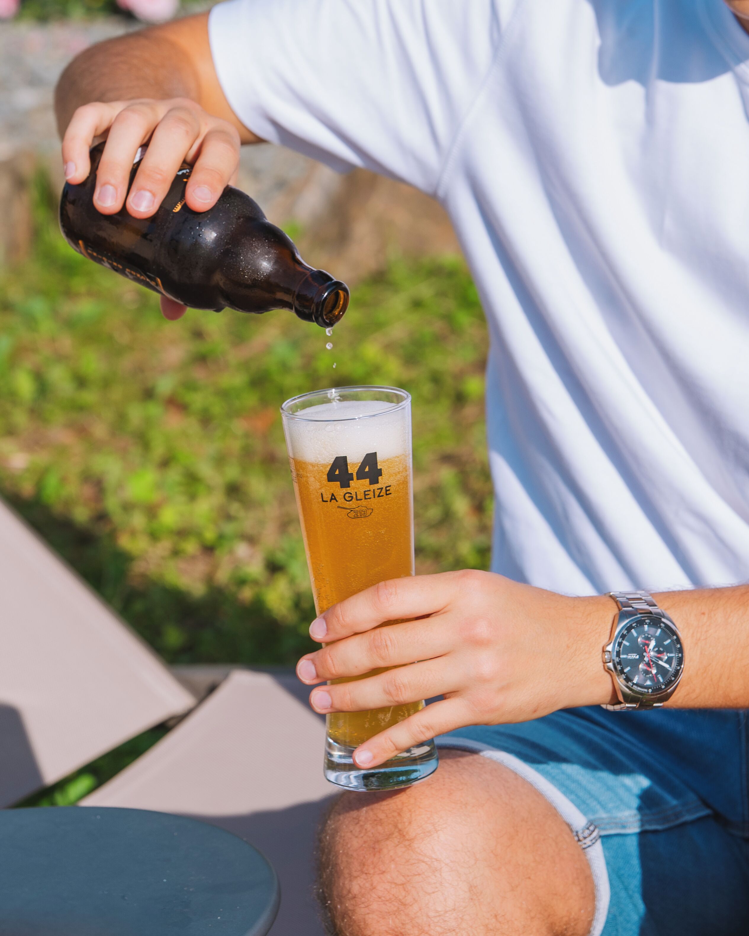 Iemand giet bier in een hoog glas met de tekst '44 LA GLEIZE', buiten.