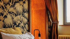 Een slaapkamer met een bed, kussens, een nachtkastje, een lamp, een raam en gordijnen.