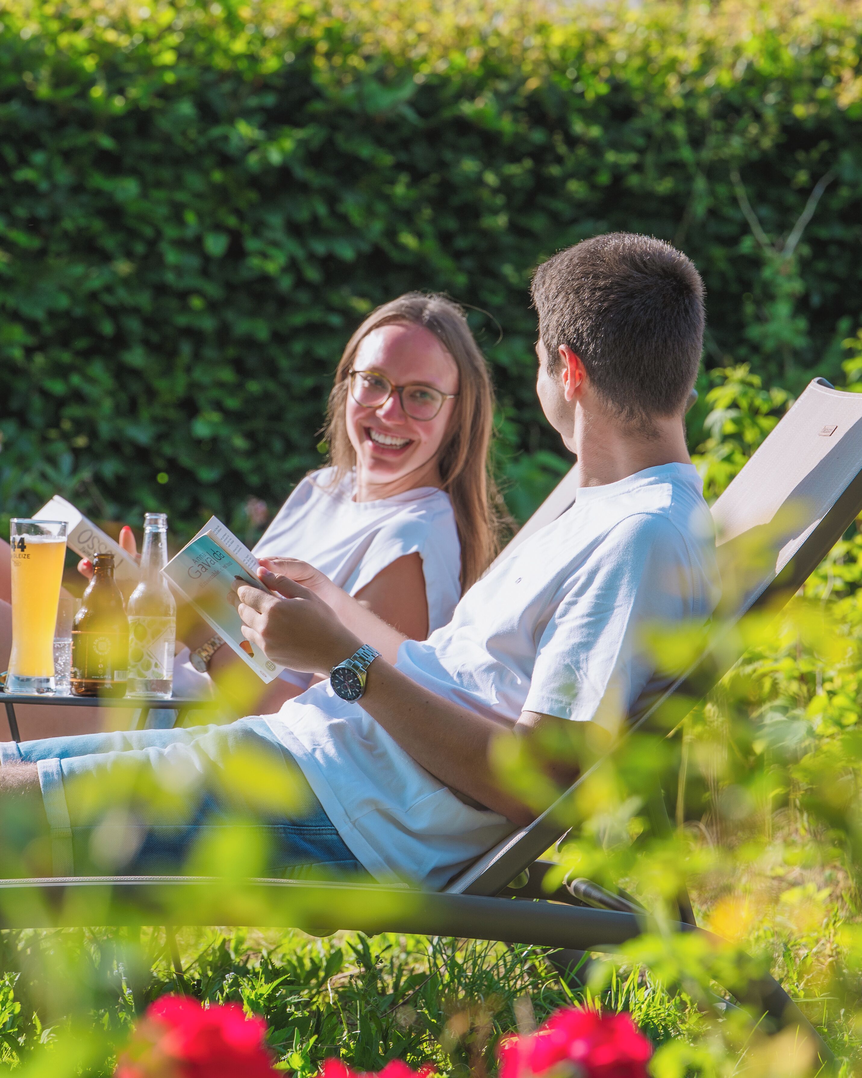 Two people sitting at an outdoor table with drinks and a menu, surrounded by greenery.
