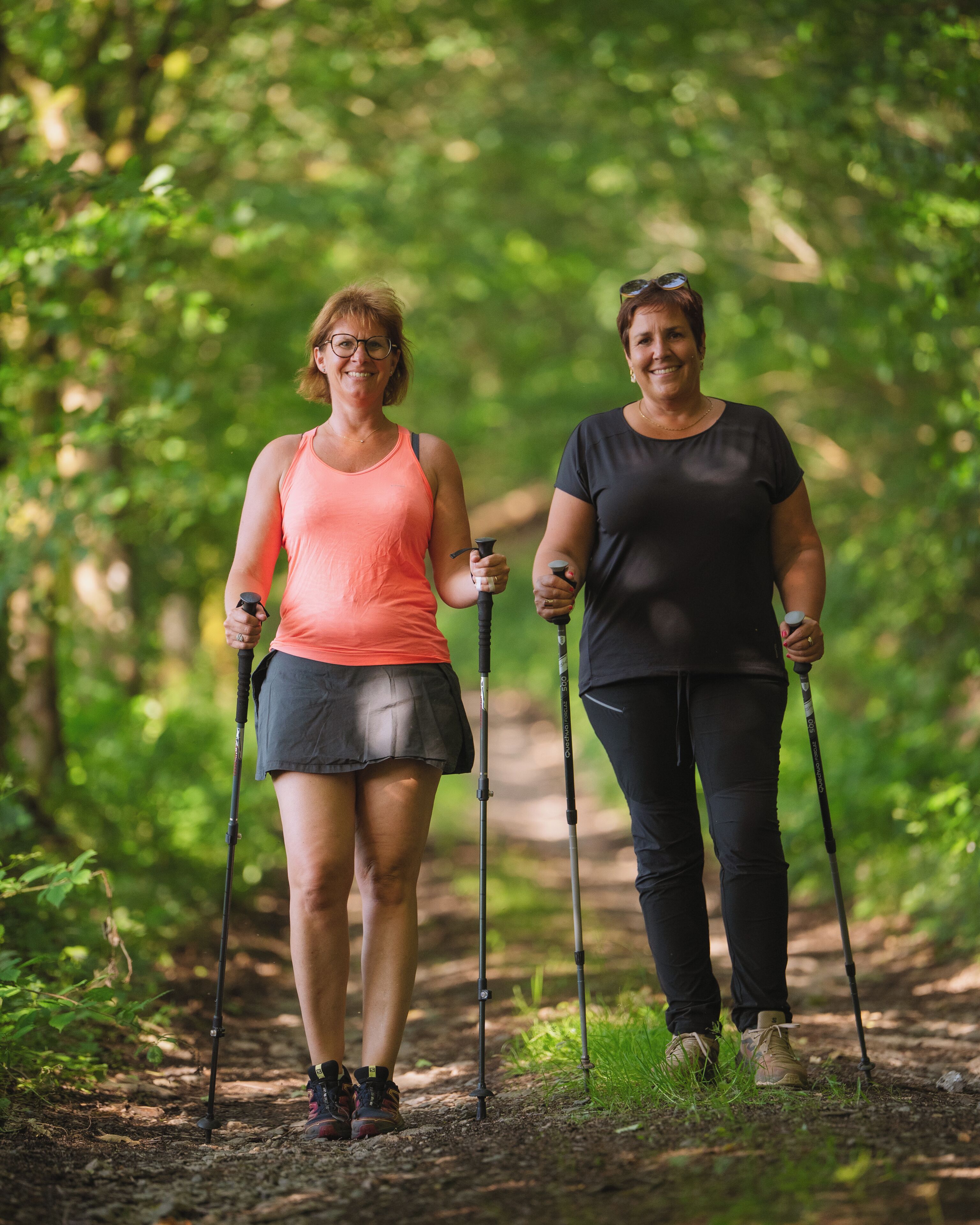 Two people hiking on a forest trail with hiking poles.