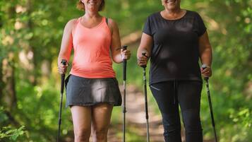 Two people hiking on a forest trail with hiking poles.