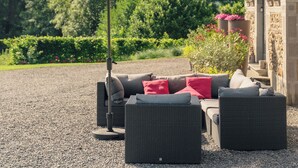 Een terras met een tafel en stoelen, een grote parasol, en een gebouw met stenen muren en een veranda.