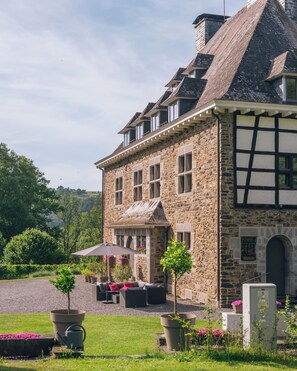 A stone building with a traditional design, featuring a courtyard with outdoor seating and potted plants. - Les chambres de la Vaulx-Renard (Stoumont)