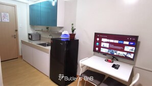 Eine kompakte Küche mit Kühlschrank, Mikrowelle und Spüle. Ein Flachbildfernseher ist an der Wand befestigt und zeigt die Benutzeroberfläche eines Streaming-Dienstes.