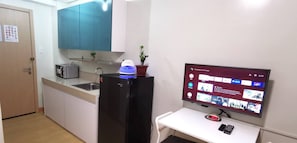 Cocina pequeña con refrigerador, microondas y pileta. Un televisor de pantalla plana está montado en la pared, mostrando la interfaz de una plataforma de streaming.