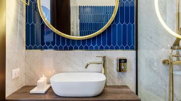 Une salle de bain avec un lavabo blanc, des robinetteries dorées, un pare-chocs bleu en carreaux et un miroir avec un cadre doré.