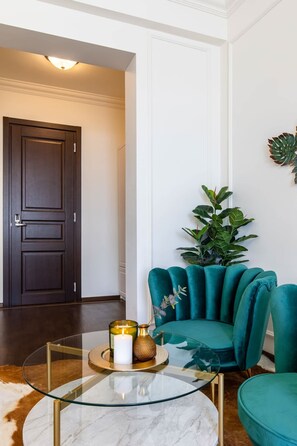 Ein modernes Wohnzimmer mit einem Glastisch, türkisfarbenen Sesseln, einer dunklen Holztür und einem Blumentopf.