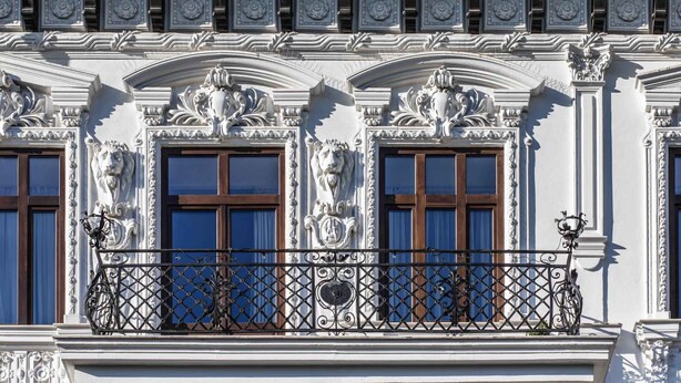 A building facade with ornate architectural details, including sculpted decorations above windows and a wrought iron balcony railing. - Old Town Luxury Suites (București)