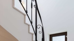 A staircase with a black wrought iron railing, a light fixture, and a window with a view. - Old Town Luxury Suites (București)