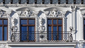 A building facade with ornate architectural details, including sculpted decorations above windows and a wrought iron balcony railing.