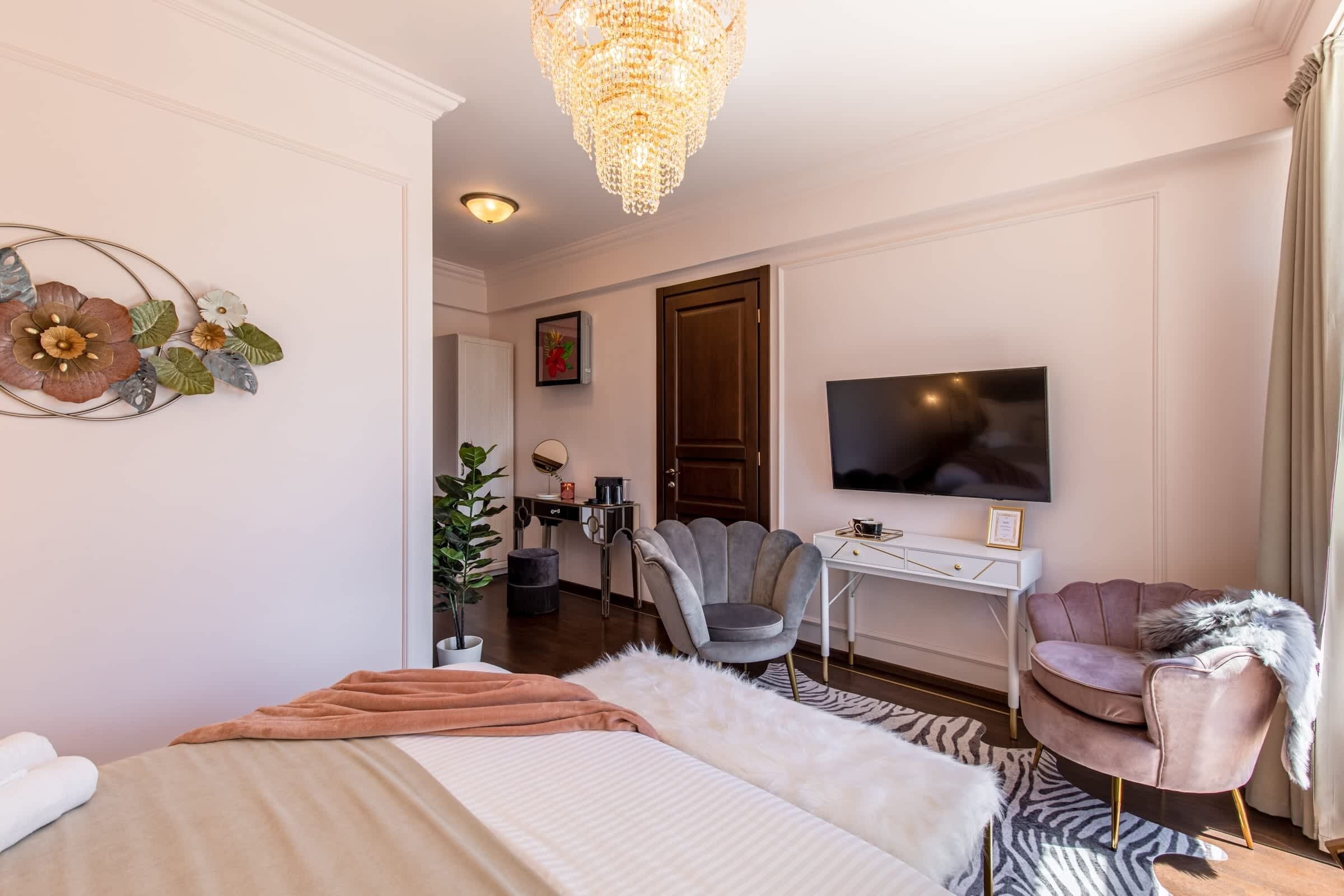 Ett hotellrum med en säng, ett skrivbord, en tv, en stol och en kristallkrona.