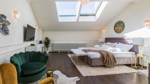 A modern bedroom with a skylight, a bed, a green armchair, and a small round table.