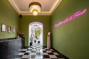 A hotel lobby with a checkered floor, a chandelier, framed certificates on the wall, and a neon sign.