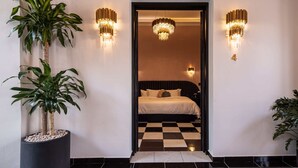 Hotellihuone, jossa on ruutukuviollinen lattia, valkoisilla lakanoilla varustettu sänky ja kaksi seinälle asennettua valaisinta.