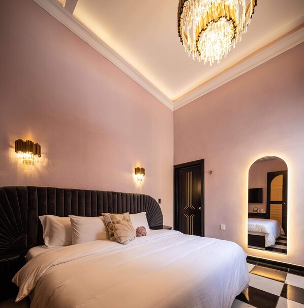 Een slaapkamer met een groot bed, een kroonluchter, wandlampen en een zwart-wit schakeerdvloer.