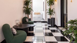 A hallway with a chandelier, potted plants, a checkered floor, and a green armchair. - HOLT Hotel De Mi Independencia King Room (Oaxaca de Juárez)