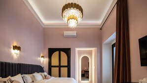A hotel room with a large bed, a chandelier, wall sconces, a flat-screen TV, and a door leading to a bathroom.