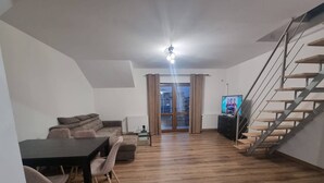 A modern living room with a dining area, a staircase, and a TV displaying a sports channel. - Rocktop Refuge In Rasnov (Rasnov)