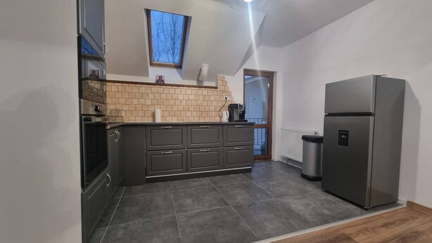 A modern kitchen with dark cabinets, a built-in oven, a coffee maker, and a stainless steel refrigerator. - Rocktop Refuge In Rasnov (Rasnov)