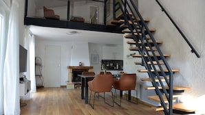 Un loft moderno con piso de madera, un área de comedor con dos sillas, una cocina con armarios blancos y una escalera en espiral negra.