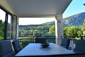 A balcony with a table and chairs, overlooking a mountainous landscape.
