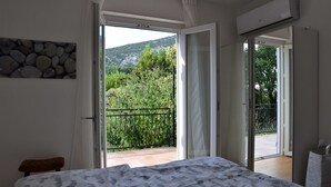Un dormitorio con una cama, un banco y vistas a un balcón con barandilla y vegetación.