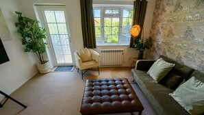 Un salon avec un pouf en cuir marron, un canapé vert, un fauteuil blanc et une plante en pot.