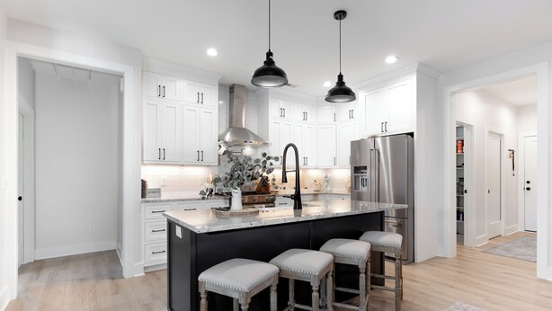 Una cocina moderna con armarios blancos, una isla grande con taburetes, electrodomésticos de acero inoxidable e iluminación colgante.