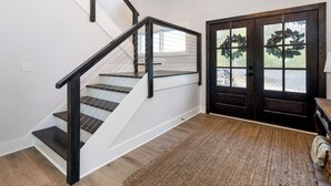 Una escalera con barandillas negras y escalones de madera, que conduce a una puerta con paneles de vidrio y una alfombra tejida en el suelo.