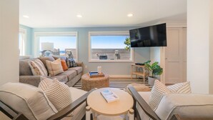 A living room with a sofa, armchairs, a coffee table, a flat-screen TV, and a large window with a view.
