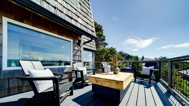 A deck with outdoor furniture, a wooden table, and a large window.