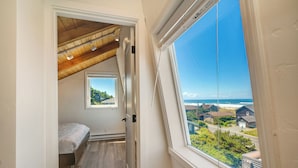 A bedroom with a skylight, a small window, and a view of the ocean and houses.