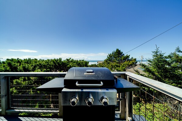 Ein Grill mit Griff und drei Reglern vor einer grünen Kulisse und blauem Himmel.