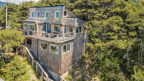 A multi-story wooden house with a balcony, surrounded by dense forest.