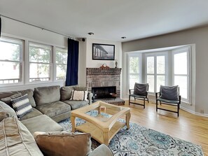 A spacious living room with a fireplace, large windows, and a cozy seating area.