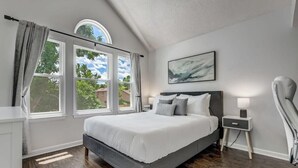 Une chambre avec un grand lit, une table de chevet, une chaise et une fenêtre avec des rideaux.