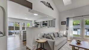 Un salon moderne avec un canapé gris, une petite table ronde et une vue sur l’extérieur grâce à de grandes fenêtres.