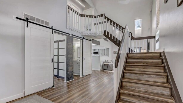 Un intérieur spacieux avec un escalier en bois, une porte coulissante et un coin cuisine à l’arrière-plan.