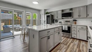 Une cuisine moderne avec des meubles gris, un îlot central et une grande fenêtre donnant sur un patio.