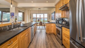 A modern kitchen with wooden cabinets, stainless steel appliances, and a large window offering a view of the outdoors. - 3BR Ski-In/Out Condo, Reno 2024, Explorer Gondola Access – Big Sky, MT (Big Sky)