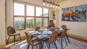 A dining area with a large window, wooden table, and chairs. There are paintings on the wall and a chandelier above the table. - 3BR Ski-In/Out Condo, Reno 2024, Explorer Gondola Access – Big Sky, MT (Big Sky)