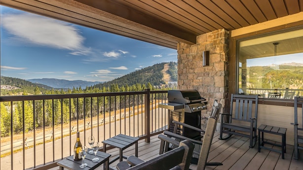 A balcony with a stone wall, a grill, and a view of a forested mountain range. - 3BR Ski-In/Out Condo, Reno 2024, Explorer Gondola Access – Big Sky, MT (Big Sky)