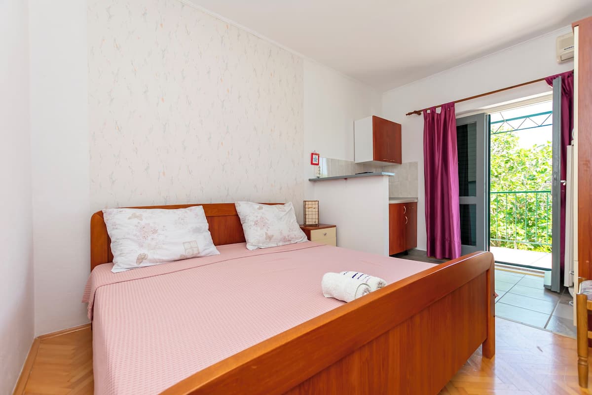 A bedroom with a wooden bed, a nightstand, a wardrobe, and a view of the outdoors through a sliding door.