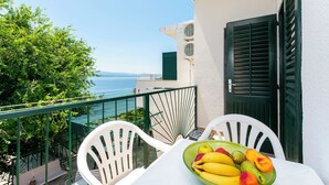A balcony with white chairs, a table with a fruit bowl, and a view of the sea.