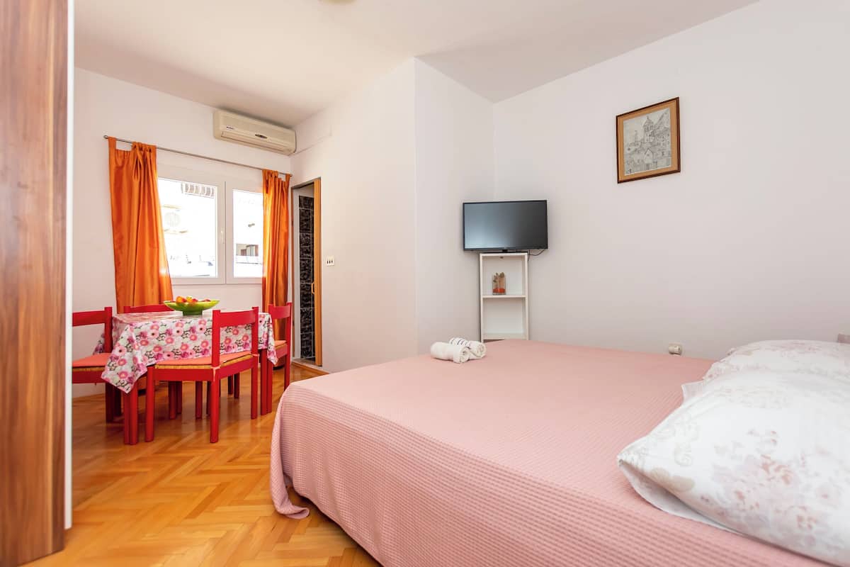 A bedroom with a bed, a TV, a painting, and a dining area with a table and chairs.