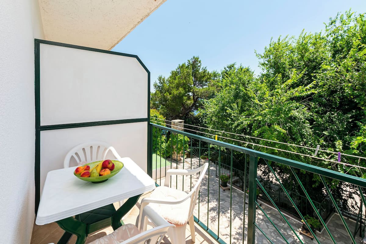 A balcony with a table and chairs, a bowl of fruit, and a view of trees.