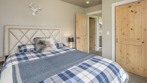 Een slaapkamer met een groot bed, een hoofdeinde versierd met een hertenbeeld, een geruite plaid en een nachtkastje met een lamp.