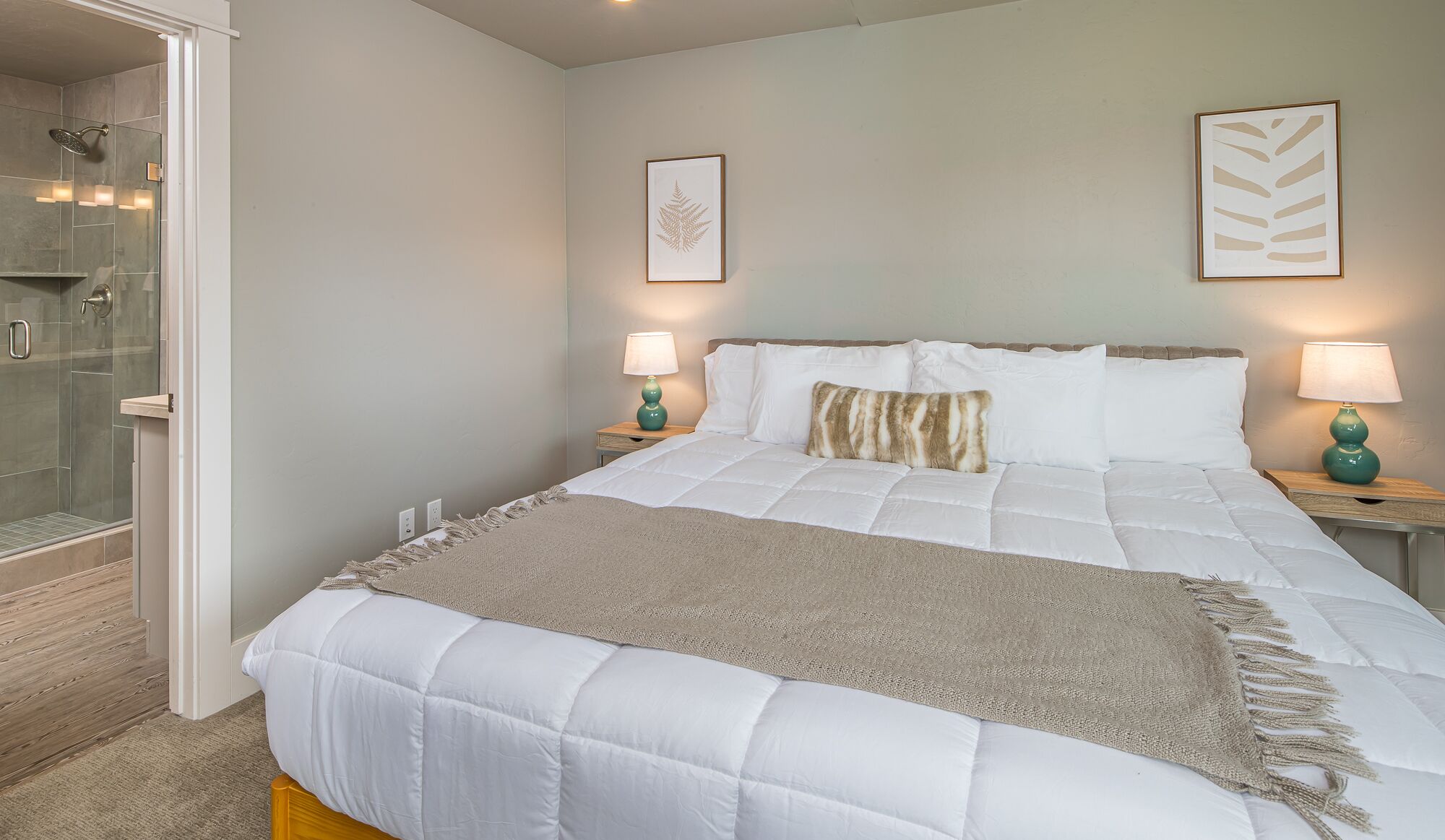 Een slaapkamer met een bed, twee nachtkastjes, een douche en een kunstwerk in een lijst aan de muur.