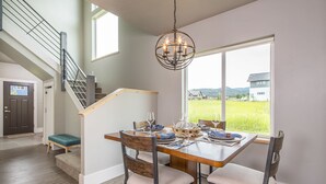 Een eetgedeelte met een houten tafel, stoelen en een kroonluchter. Er is een trap met een leuning die naar een ander niveau leidt.