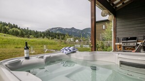 Een hottub met een fles wijn en glazen, met uitzicht op een bergachtig landschap.